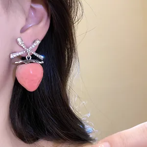 Detailed view of sweet pink strawberry stud earrings with crystal bow on model's ear