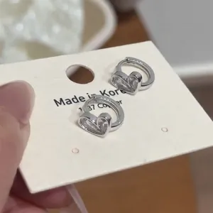 Macro detail of silver heart-shaped zircon hoop earrings displayed on a cream jewelry card.