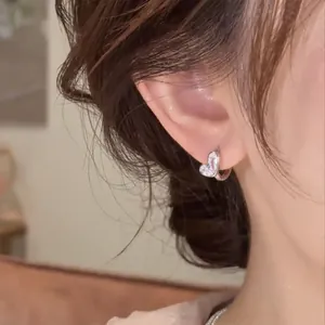 Detailed close-up of a delicate silver heart-shaped earring with sparkling zircon on ear