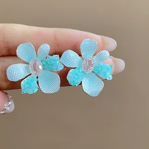 Detailed close-up of light blue glass flower earrings with sparkling central zircon stones.