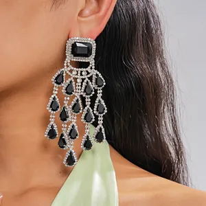 Close-up of exaggerated square and water drop tassel earrings with black gemstones.