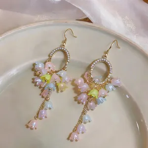 Close-up detail view of elegant floral tassel earrings with colorful lilies and gold hooks.