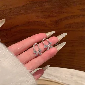 Delicate sparkling rhinestone butterfly bow pearl stud earrings held for size detail.