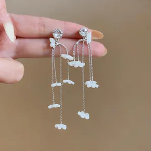 Detailansicht langer Quastenohrringe mit weißen Gänseblümchen aus Harz und Kristallen.