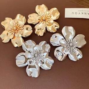 Vintage oversized metallic flower stud earrings in gold and silver on leather surface