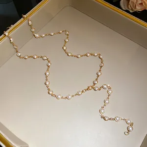 Detailed view of a gold-tone necklace with white beads in a beige jewelry tray