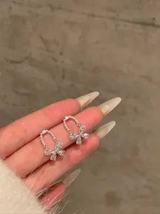 Close-up view of sparkling crystal bow earrings featuring delicate pearl loop detailing on fingers