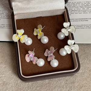 Detalle detallado de elegantes pendientes de flores de esmalte con grandes perlas blancas