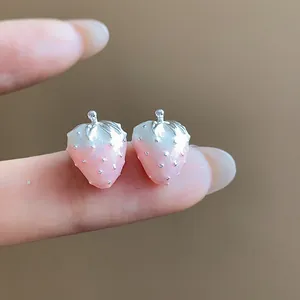Detailed close-up of pink and white gradient strawberry stud earrings on a finger