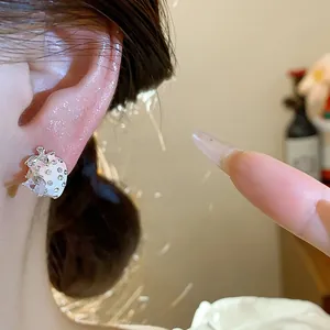 Close-up of a delicate strawberry stud earring with zircons and enamel finish on ear.