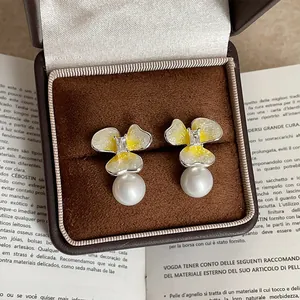 Primer plano de pendientes de flor amarilla con elegantes perlas colgantes en estuche.