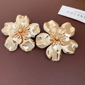 Detailed view of oversized glossy gold flower stud earrings on leather background.