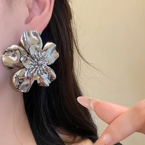 Close-up detail of oversized silver metallic flower stud earring with shiny finish