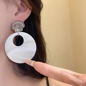 Detailansicht eines Muschel-Ohrrings im Sommer-Resort-Stil mit großer weißer Scheibe