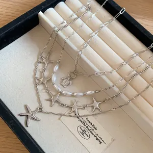 Close-up of layered silver necklace with starfish, turtle charms and pearls