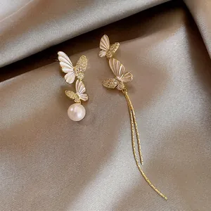 Macro view of gold butterfly asymmetrical earrings with pearl and tassel details