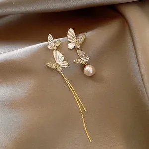 Macro detail of luxury asymmetric butterfly earrings with gold tassels and pearl drops