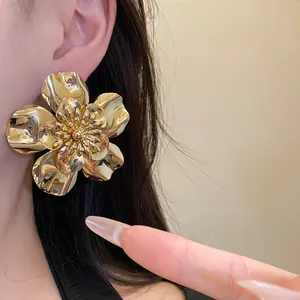 Detailed view of oversized gold metallic flower stud earring worn on model's ear