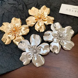 Close-up of metallic flower earrings in gold and silver with shiny glossy finish.