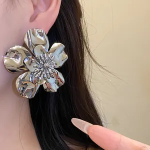 Macro view of oversized shiny silver metallic flower earrings with textured petals worn on ear