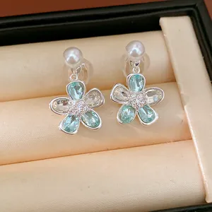 Primo piano di orecchini a fiore argentati con cristalli blu e perle in scatola.