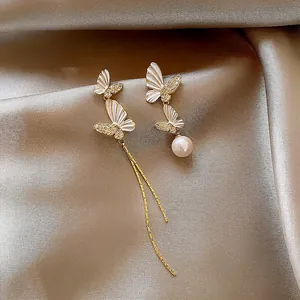 Close-up detail of asymmetric butterfly earrings with long gold tassels and a pearl.