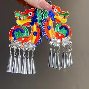 Detailed macro view of vibrant embroidered dragon earrings featuring silver metal tassels
