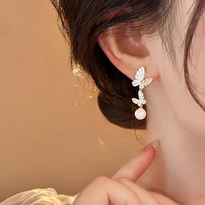 Close-up detail of resort style butterfly pearl tassel earring on female model's ear