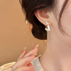 Detailed close-up of elegant gold butterfly tassel earrings worn by a model.