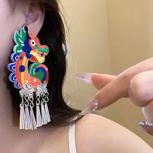 Close-up of colorful embroidered dragon earring with silver metallic tassels on model.