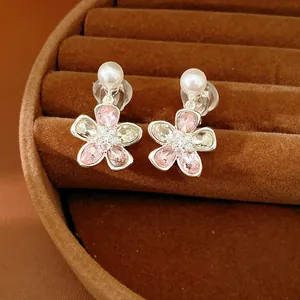 Dettaglio degli orecchini a clip a fiore con cristalli rosa e perle su vassoio marrone