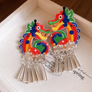 Detail view of colorful embroidered dragon earrings with silver tassels in a box.