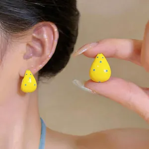 Detalle de pendientes en C de esmalte amarillo con lunares azules puestos en la oreja
