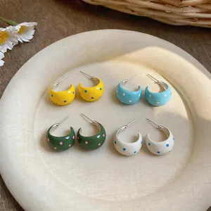 Primer plano de cuatro pares de pendientes de aro en forma de C con esmalte y lunares.