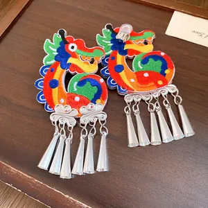 Detail shot of colorful embroidered dragon clip earrings with silver metallic tassels