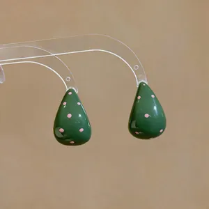 Primer plano detallado de pendientes de gota verdes con lunares rosas y acabado brillante