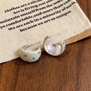 Vista detallada de pendientes en forma de C de esmalte crema con lunares azules sobre madera.
