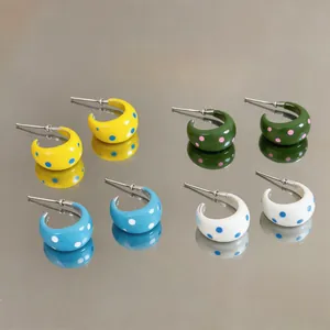 Detalle de pendientes de aro esmaltados con lunares de colores en superficie reflectante