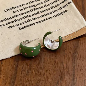 Primer plano de pendientes en C de esmalte verde con lunares rosas sobre fondo vintage