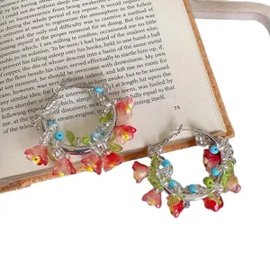 Orecchini a cerchio con fiori di perline e ciondoli rossi su sfondo di un libro vintage.
