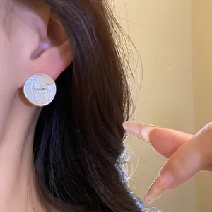 Vintage matte silver round stud earrings featuring an embossed horse coin design on ear.