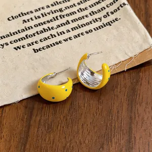 Primer plano de pendientes de aro en C de esmalte amarillo con lunares y agujas de plata