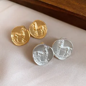 Detailed view of matte gold and silver round stud earrings featuring a raised horse motif.