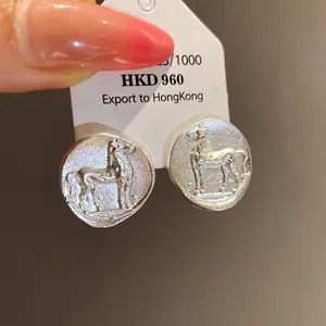 Macro view of matte silver round stud earrings featuring an embossed pony design.