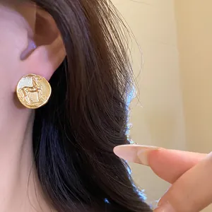 Close-up of vintage matte gold circular stud earring featuring a horse motif on ear.