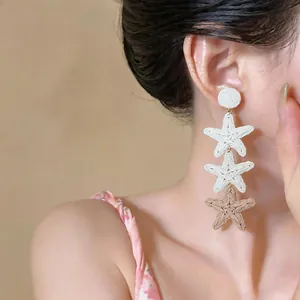 Close-up of bohemian raffia woven star dangle earrings worn on a model's ear