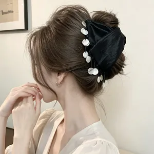 Detailed view of an elegant black satin hair claw clip with shell tassels on model.