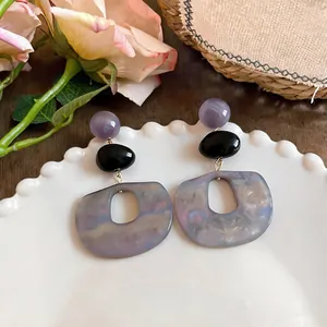 Nahaufnahme von Vintage-Ohrringen aus lila Marmor-Acetat mit geometrischen Ovalen auf Teller