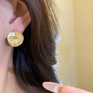 Close-up view of a vintage matte gold round stud earring featuring a horse pattern
