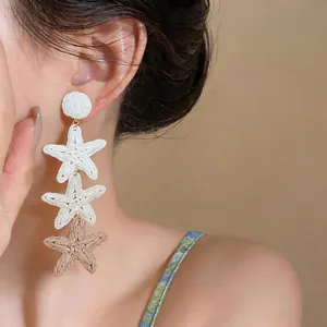 Close-up of elegant summer raffia starfish tassel earrings with white and tan woven details